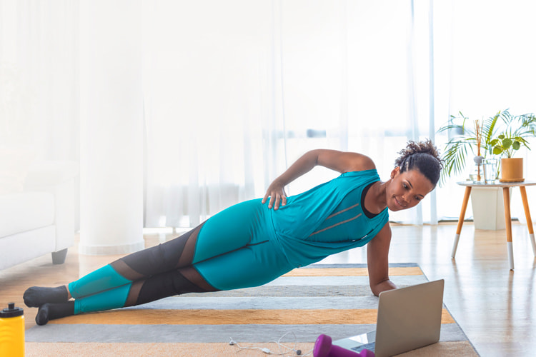 Woman in workout clothes holding a side plank in front of an open laptop