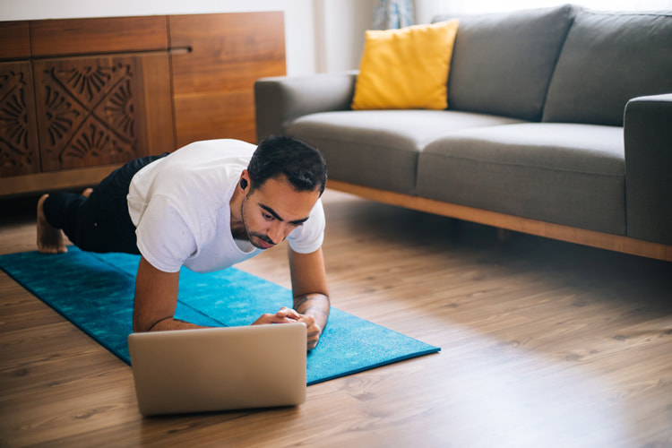 man in workout clothing doing a plank pose on floor with a laptop