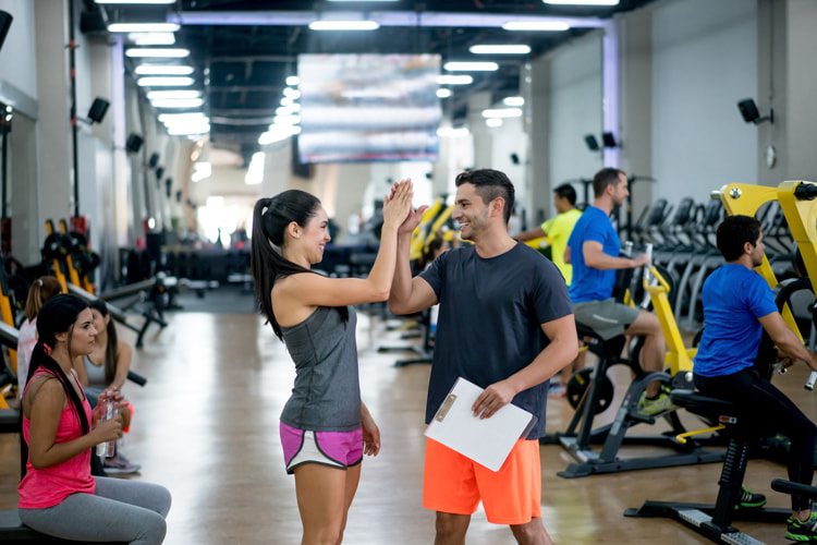man and woman in workout clothing clap their hands in a high five in busy fitness center